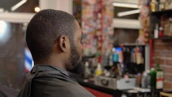 A young man is sitting in a hairdresser's chair in front of a mirror before a haircut video