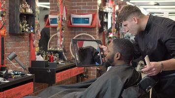de frisör visar de klient de resultat av de frisyr och rakning i de hand spegel video