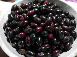 Jamblang or duwet or juwet or java plum or jaam or jamun or black jam or giant duhat on green bowl in isolated background in white. Tangerine and sweet taste. photo