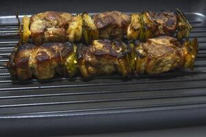 Meat and pepper skewers in a non-stick pan. Generally a skewer is made up of pieces of meat or fish interspersed with onion, pepper, mushrooms, etc. photo