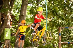 Child in forest adventure park. Kids climb on high rope trail. Agility and climbing outdoor amusement center for children. Little girl playing outdoors. School yard playground with rope way. photo