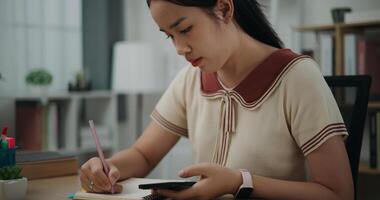 Selective focus, Female writer sitting at desk writing noting information to diary from smartphone at home, creative thoughts to journaling, idea and inspiration photo