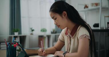 Selective focus, Side view, Female writer sitting at desk thinking idea holding pen making notes in diary while working on tablet for online learning at home, creative thoughts to journaling photo