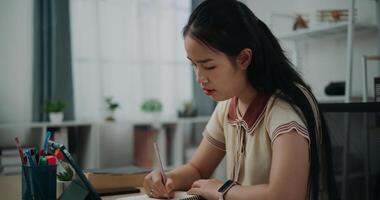 Selective focus, Side view, Female writer sitting at desk writing notes while working on tablet for online learning at home, creative thoughts to journaling, idea and inspiration photo