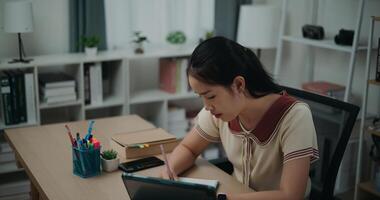 Selective focus, Side view,Female writer sitting at desk writing notes while working on tablet for online learning at home, creative thoughts to journaling, idea and inspiration photo