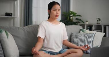 Selective focus, Young attractive woman is using laptop to watch online yoga lessons sitting on sofa with eyes closed do meditation in the living room at home photo