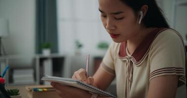 Selective focus, Side view, Female writer wear wireless headphones sitting at desk while writing notes at home, creative thoughts to journaling, idea and inspiration photo