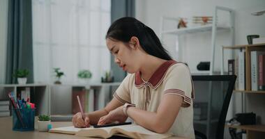 Side view, Selective focus, Female writer sitting at desk writing information on diary notebook while reading book at home, creative thoughts to journaling, idea and inspiration photo