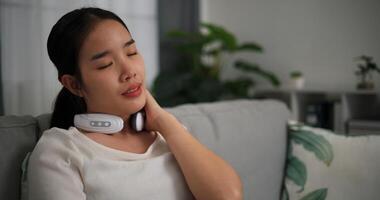 Selective focus, Relaxed young woman wear automatic massage neck with eyes closed,sitting on sofa at home ,relaxing body and mind alone in the living room, breathing fresh air, photo