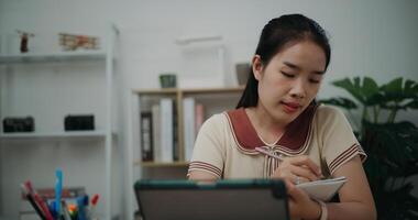 Selective focus, Front view, Female writer sitting at desk thinking idea holding pen making notes in diary while working on tablet for online learning at home, creative thoughts to journaling photo