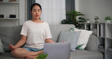 Selective focus, Young attractive woman is using laptop to watch online yoga lessons sitting on sofa with eyes closed do meditation in the living room at home photo