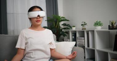 Selective focus, Relaxed young woman wear VR goggles meditating doing a lotus pose at home sitting on sofa and experiencing virtual reality in living room photo