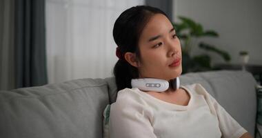 Selective focus, Relaxed young woman wear automatic massage neck sitting on sofa at home ,relaxing body and mind alone in the living room, breathing fresh air, photo