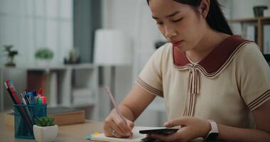 Selective focus, Female writer sitting at desk writing noting information to diary from smartphone at home, creative thoughts to journaling, idea and inspiration photo