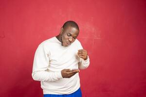 Young african american man with surprised facial expression hold smartphone in his hands, typing message, chatting with friends in social networks photo