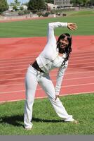 Young black woman stretching at track on grass photo