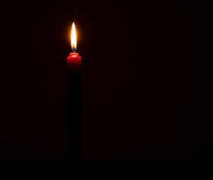 Single burning candle flame or light glowing on a small red candle on black or dark background on table in church for Christmas, funeral or memorial service with copy space. photo