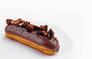 Eclair with Chocolate Cream and Hazelnuts on White Plate photo