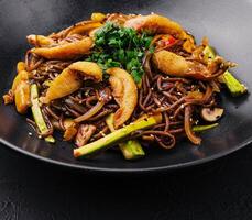 Chinese fried buckwheat pasta with meat on black plate photo