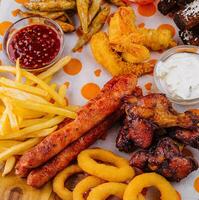 francés papas fritas patatas con cebolla anillos, salchichas, picatostes y picante pollo piernas foto