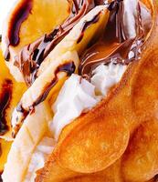 hong kong or bubble waffle with whipped cream, chocolate and bananas close up photo