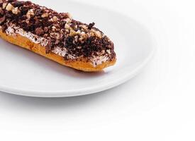 eclair with chocolate and nuts on a white plate photo