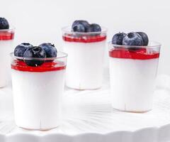Glass cup of yogurt with blueberries on white table photo