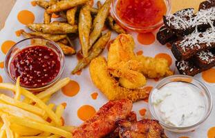 french fries potatoes with onion rings, sausages, croutons and spicy chicken legs photo