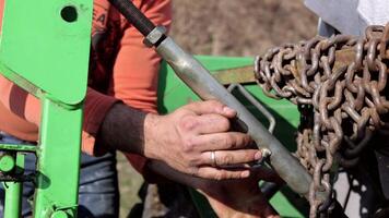 A young farmer turns the handle and adjusts the plow to work. He does this to set up the machine. He needs to adjust the plow to loosen the soil and prepare it for sowing. video