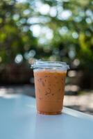 Ice Thai milk tea in a plastic cup on wooden table against a natural background. photo