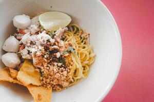 Egg noodles dried egg noodles with lime, minced pork, meatballs, and fried dumplings in white bowl photo