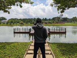 hombre estar en frente de el camino lago en abajo ciudad. el foto es adecuado a utilizar para aventuras contenido medios de comunicación, naturaleza póster y bosque antecedentes.