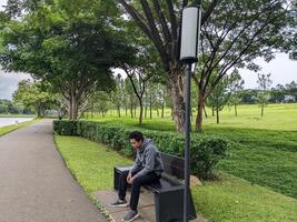 hombre sentar en el verde parque abajo ciudad. el foto es adecuado a utilizar para calma disfruté actividad, ocio actividad y parque antecedentes.