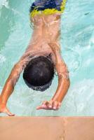 Happy Indian boy swimming in a pool, Kid wearing swimming costume along with air tube during hot summer vacations, Children boy in big swimming pool. photo