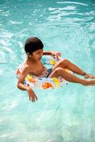 Happy Indian boy swimming in a pool, Kid wearing swimming costume along with air tube during hot summer vacations, Children boy in big swimming pool. photo