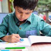 Smart Indian little boy perform thumb painting with different colourful water colour kit during the summer vacations, Cute Indian Kid doing colourful thumb painting drawing on wooden table photo