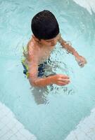 Happy Indian boy swimming in a pool, Kid wearing swimming costume along with air tube during hot summer vacations, Children boy in big swimming pool. photo