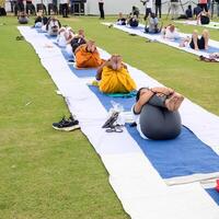 New Delhi, India, June 21, 2023 - Group Yoga exercise session for people at Yamuna Sports Complex in Delhi on International Yoga Day, Big group of adults attending yoga class in cricket stadium photo