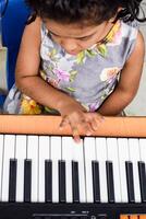 Asian cute girl playing the synthesizer or piano. Cute little kid learning how to play piano. Child's hands on the keyboard indoor. photo