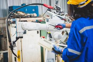 Mecánico del equipo de ingenieros que usa un brazo robótico controlador de computadora para soldar acero en el taller de la fábrica de acero. software de programación de robots industriales para tecnología de fabricación automatizada foto