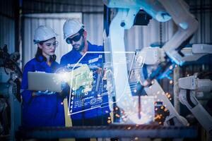 dos ingenieros mecánicos que usan un brazo robótico controlador de computadora para soldar acero en el taller de la fábrica de acero. software de programación de robots industriales para tecnología de fabricación automatizada foto