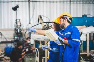 Mecánico del equipo de ingenieros que usa un brazo robótico controlador de computadora para soldar acero en el taller de la fábrica de acero. software de programación de robots industriales para tecnología de fabricación automatizada foto