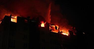 brand laaiend in appartement gebouw. brandend huis is overspoeld in vlammen Bij nacht. brandweerlieden blussen met water video