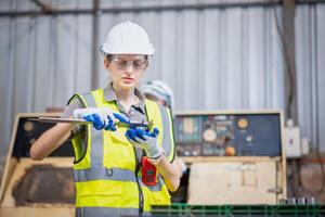 Caucasian female engineering wearing PPE inspecting auto robot lathe machine to drill components at steel structure industry. photo