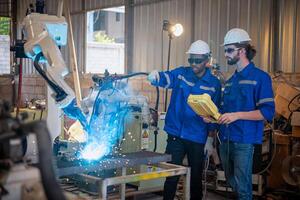 Two engineers mechanic using computer controller Robotic arm for welding steel in steel factory workshop. Industry robot programming software for automated manufacturing technology . photo