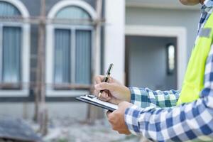 el inspector o ingeniero está inspeccionando la construcción y el aseguramiento de la calidad de la nueva casa usando una lista de verificación. ingenieros o arquitectos o contratistas trabajan para construir la casa antes de entregársela al propietario foto