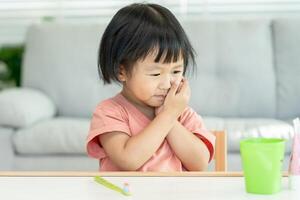 little asian girl presses hand to cheek, suffers from pain in tooth. Teeth decay, dental problems, child emotions and facial expression, oral health care, reducing sweets, fluorine coating photo