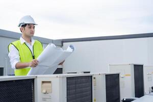 Asian maintenance engineer works on the roof of factory. contractor inspect compressor system and plans installation of air condition systems in construction. Blueprint, inspector, control photo