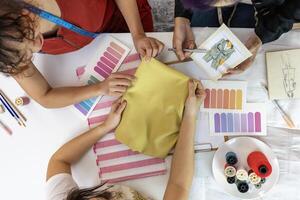 Team of fashionable freelance dressmakers and customer choosing design and fabric color for new custom dress while working in artistic workshop studio for fashion design and clothing business industry photo