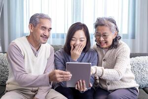 Asian family reunion of senior father, mother and daughter sitting on couch with happy smile in retirement home while looking at old nostalgic photo in the past